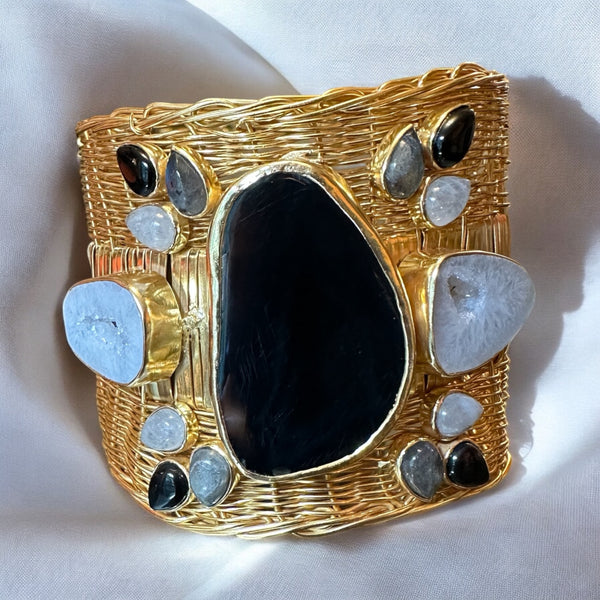 A gold-plated brass bangle featuring a central black obsidian stone with labradorite and moonstone gemstone accents.