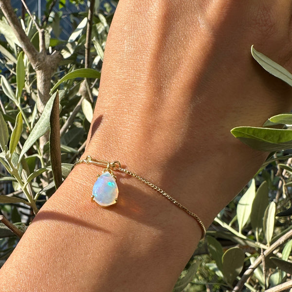 A person's wrist wearing a gold-plated bracelet with an opal teardrop gemstone.
